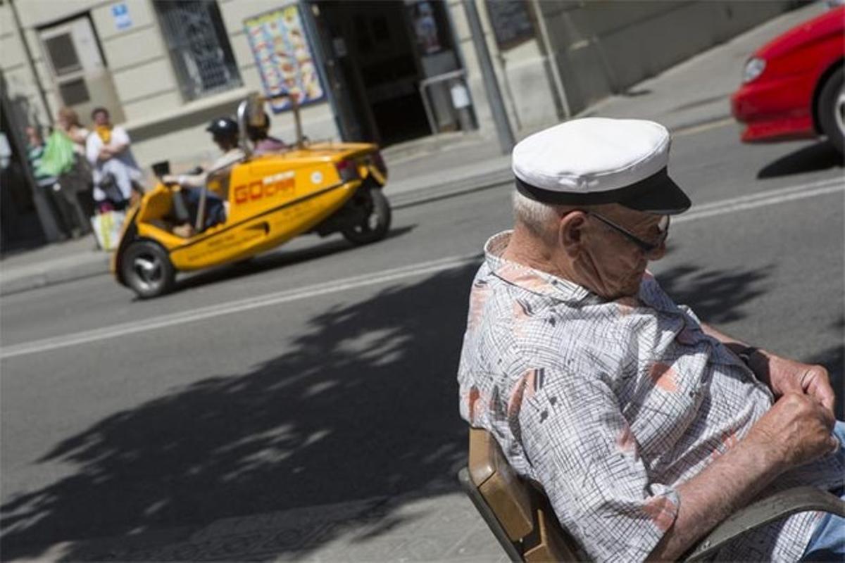 Dos turistes condueixen un Go Car en un carrer de la Barceloneta, mentre un veí pren el sol.