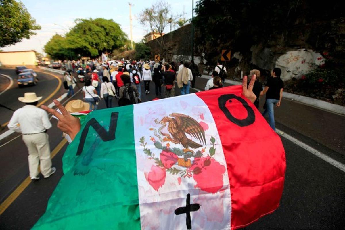 Un home aguanta una bandera mexicana tacada de pintura vermella durant la marxa per la pau que arribarà a Ciutat de Mèxic diumenge. Un home aguanta una bandera mexicana tacada de pintura vermella durant la marxa per la pau que arribarà a Ciutat de Mèxic diumenge.