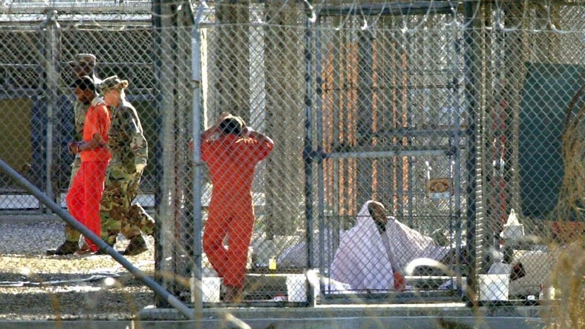 Un recluso de Guantánamo, escoltado por dos guardias en el penal, junto a otros dos presos en sus celdas, el 15 de marzo del 2002.