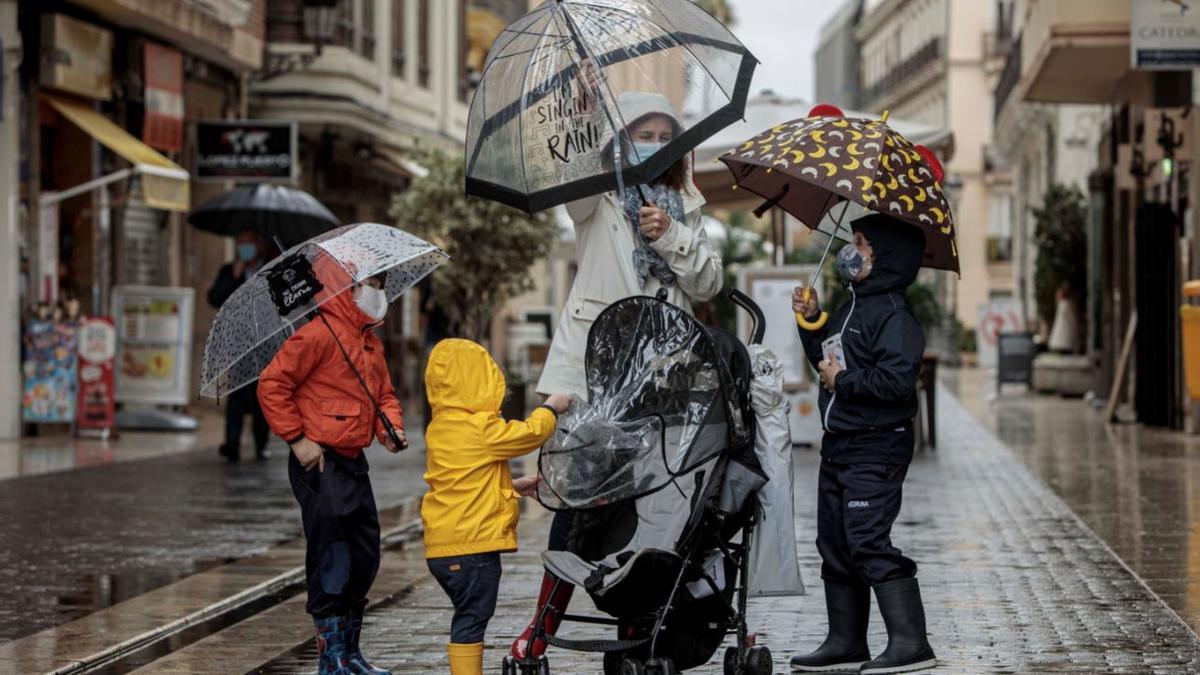 Una mujer con tres menores se protegen de la lluvia con paraguas y chubasqueros en una céntrica calle de València