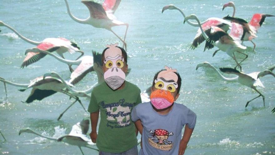 La imagen muestra a dos niños participantes en un taller de confección de máscaras con la imagen de los flamencos del parque Salinas y Arenales de San Pedro del Pinatar.