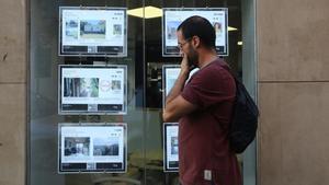 Un joven mirando ofertas de pisos de alquiler en los expositores de una inmobiliaria de Barcelona.