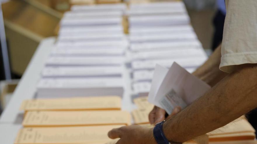 Un hombre coge una papeleta en una mesa electoral.