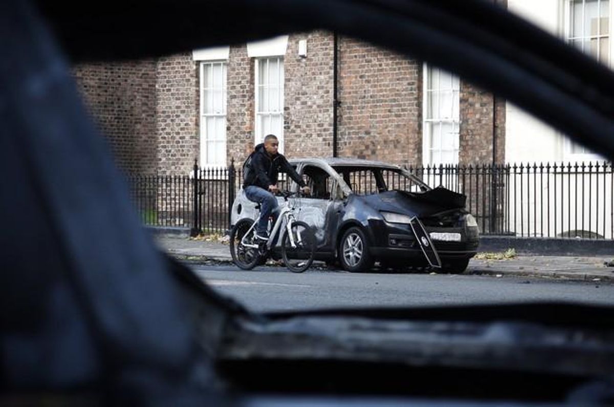 Un ciclista passa al costat d’un dels cotxes incendiats durant els disturbis a Liverpool (Anglaterra).