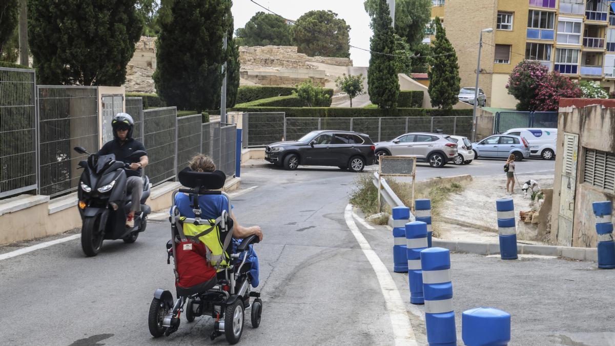 Una vecina de La Albufereta pasa junto a una moto ante la falta de aceras adaptadas.