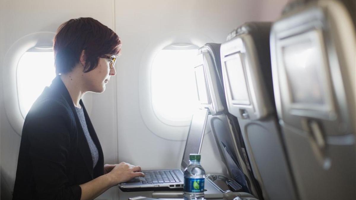 Una usuaria navega por internet a través de wifi en un avión con su portátil.