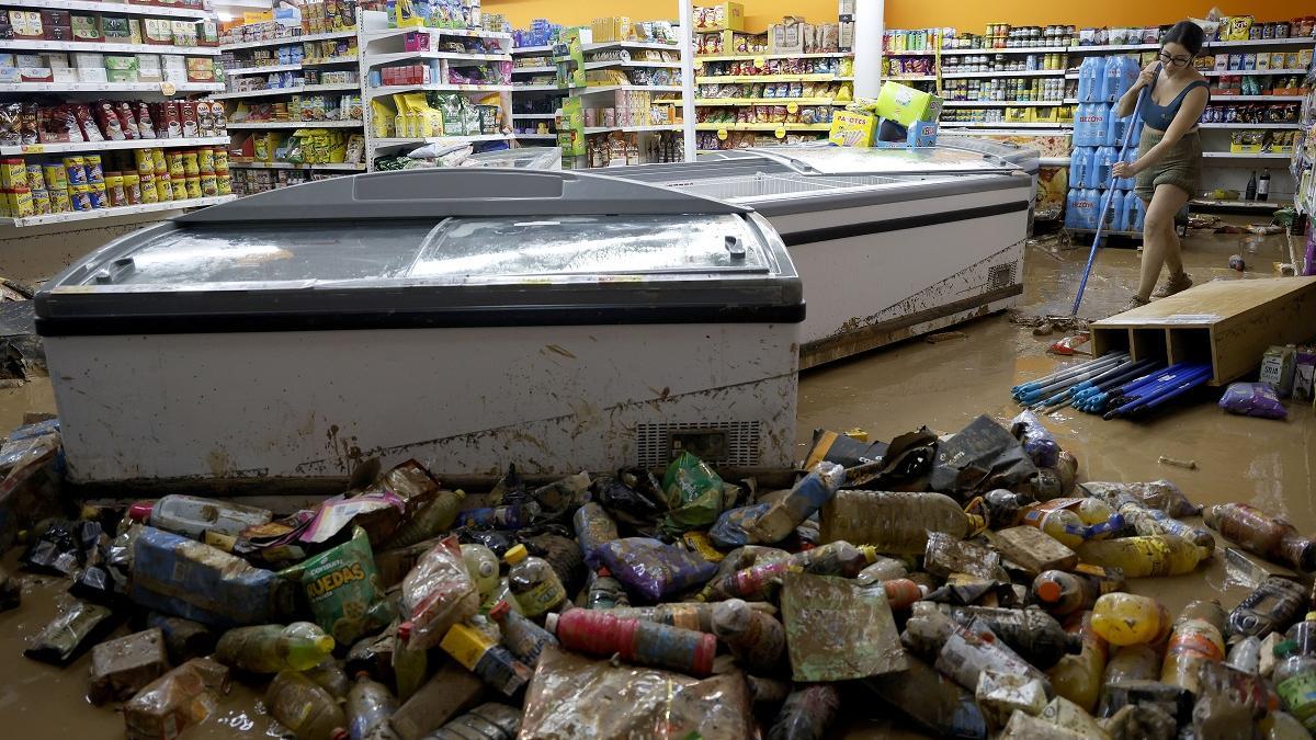 Una mujer limpia su comercio afectado por las inundaciones del 29 de octubre