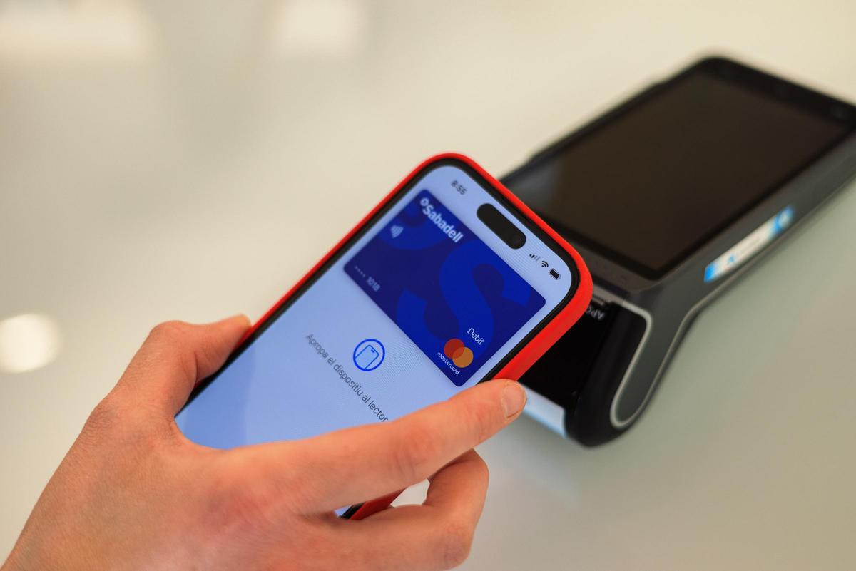 Una persona pagant amb una targeta del Banc Sabadell al telèfon mòbil en un establiment
