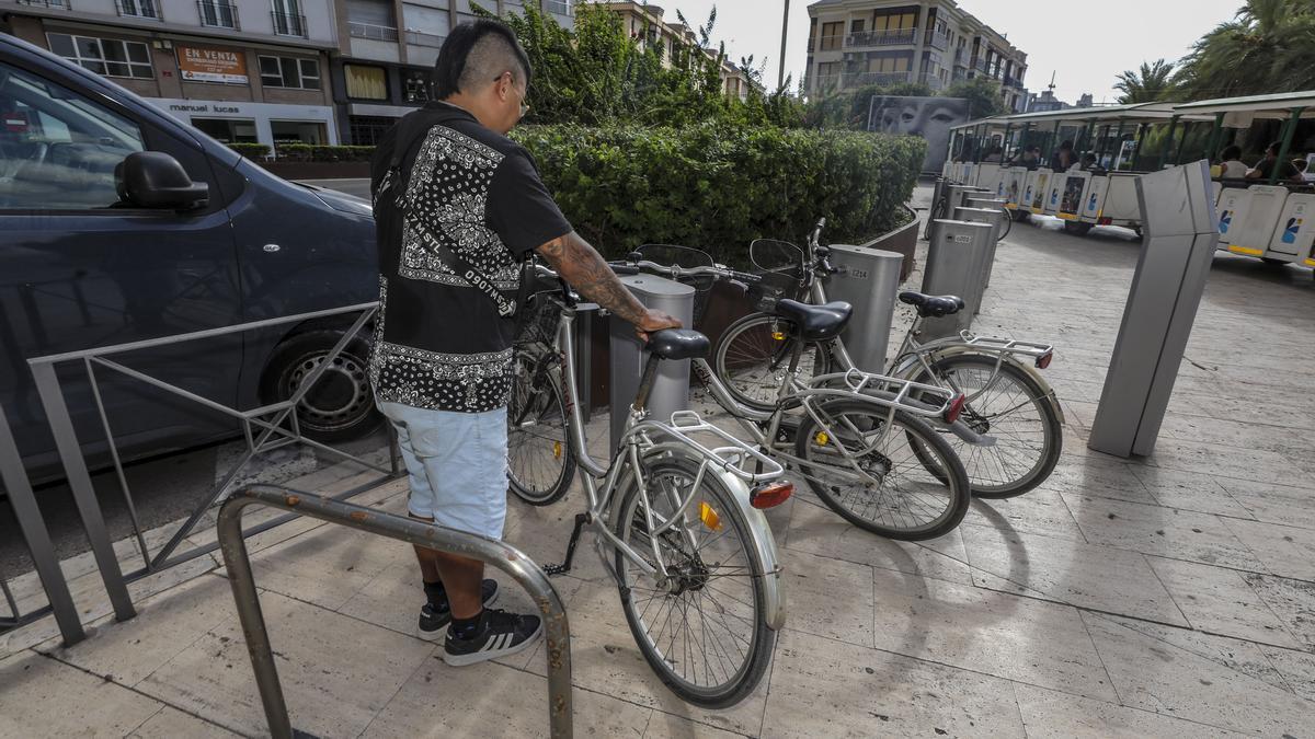 Un usuario coge una de las bicicletas de BiciElx frente al tren turístico que recorre la ciudad.  | ANTONIO AMORÓS