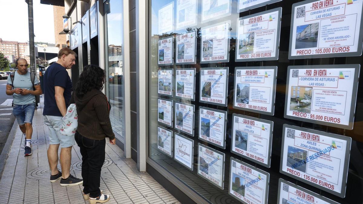 Dos personas contemplan el escaparate de una inmobiliaria avilesina.