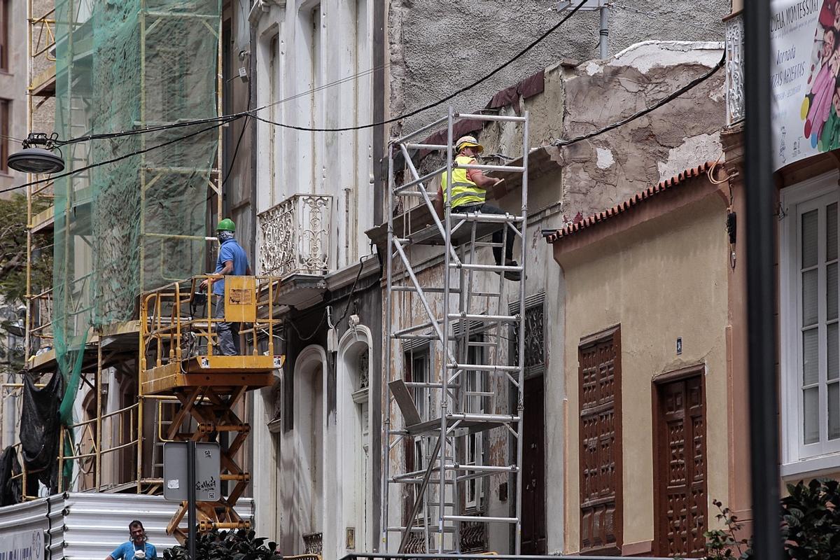 Varios obreros rehabilitan la fachada de una vivienda.