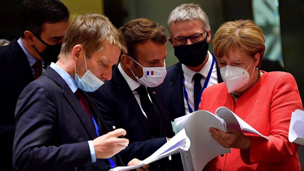 Pedro Sánchez (izquierda), Emmanuel Macron (centro) y Angela Merkel (derechan) examinan los documentos del acuerdo sobre el fonde de reconstrucción, el 20 de julio del 2020 en Bruselas