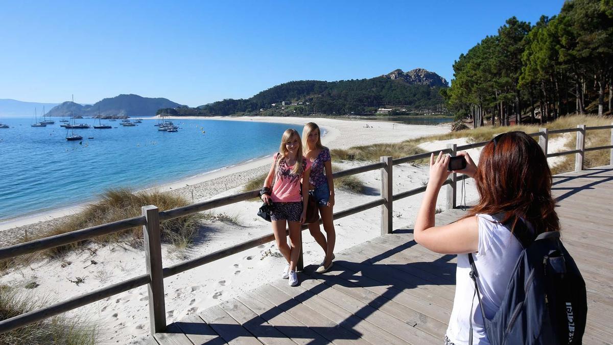 Foto de archivo de turistas sacando una foto en las islas Cíes con la playa de Rodas al fondo.