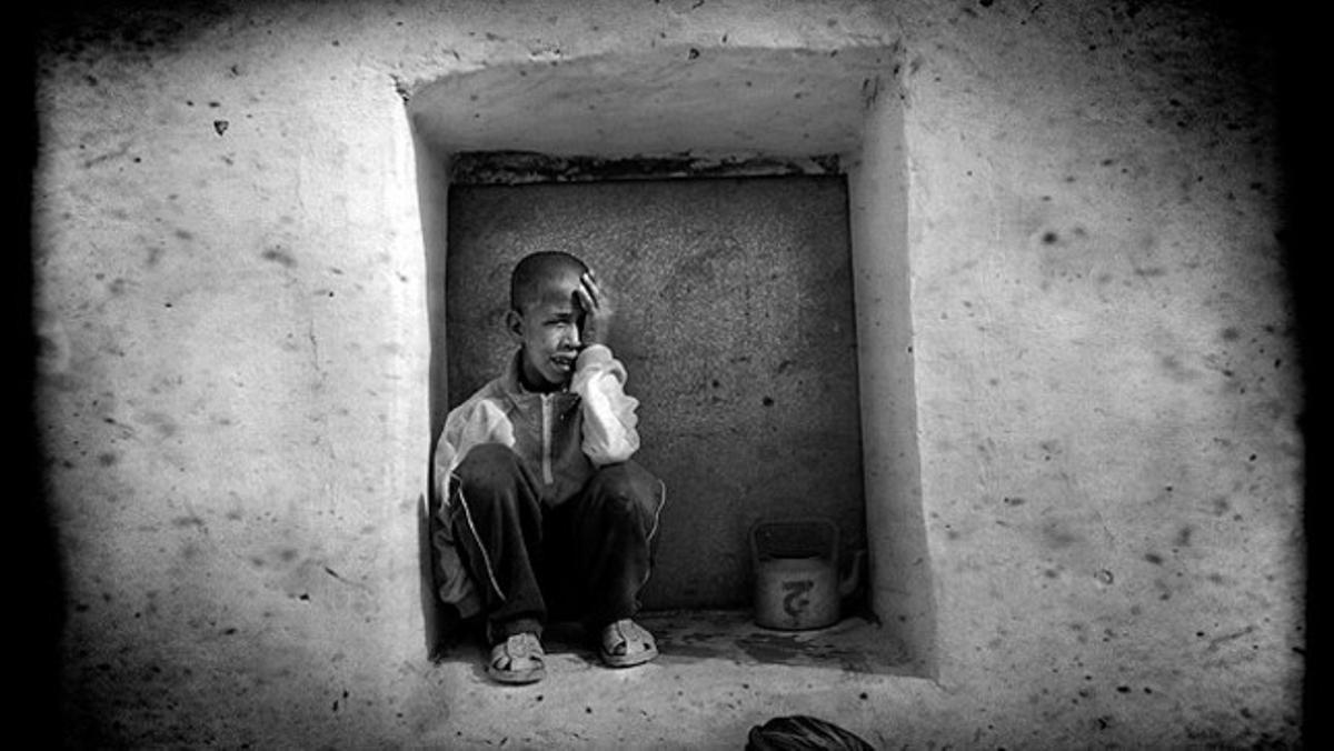 Un nen plora assegut en una finestra.