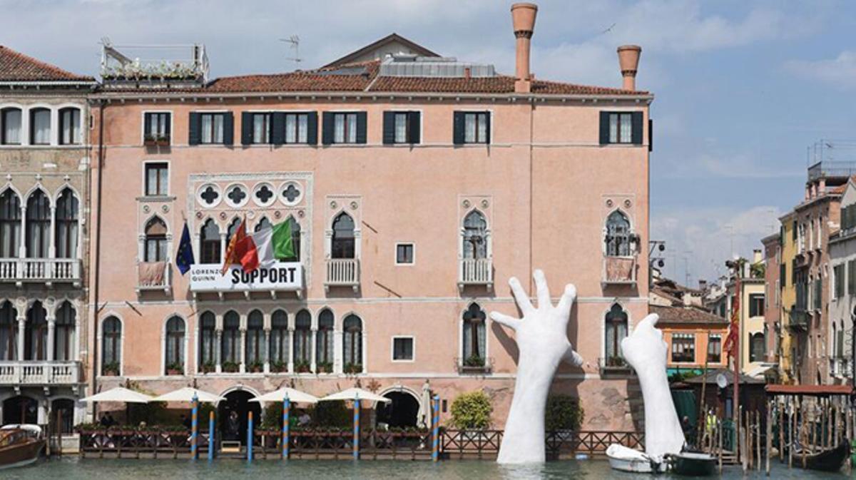 Unes mans, obra de Lorenzo Quinn, aguanten un palau en perill a Venècia.