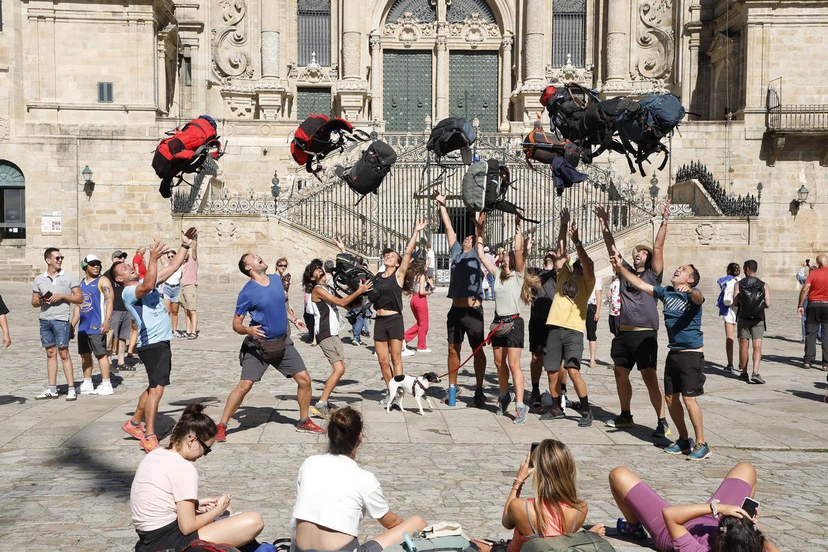 Un grupo de peregrinos hace volar sus mochilas a su llegada a la Praza do Obradoiro