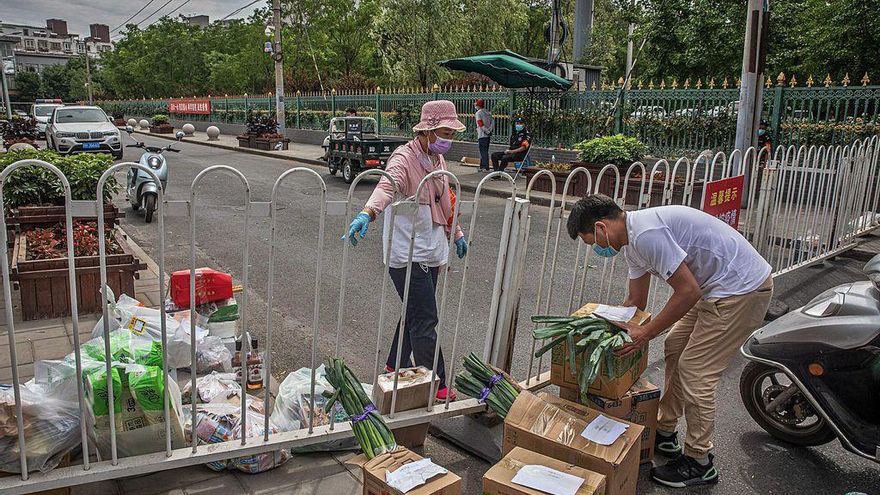 Un hombre lleva cajas de alimentos hasta la valla que delimita una zona confinada de Pekín.