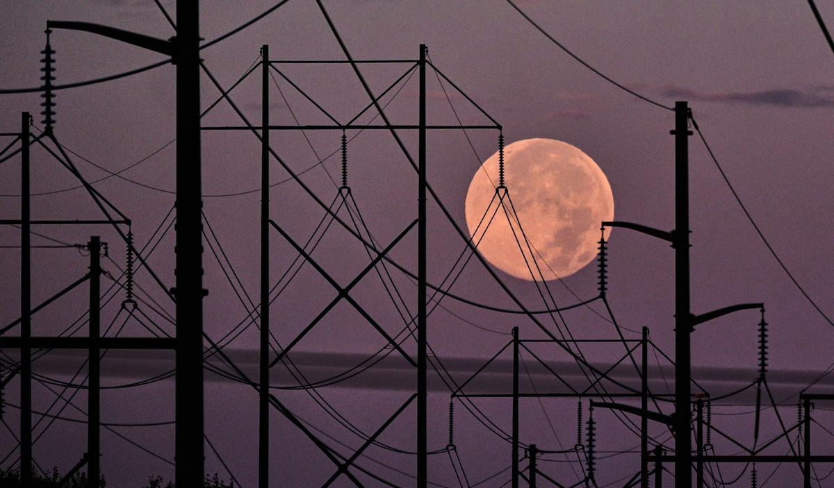 The full harvest super moon sets behind electrical power transmission lines at dawn, Tuesday, Oct. 7, 2025, in East Derry, N.H. (AP Photo/Charles Krupa)