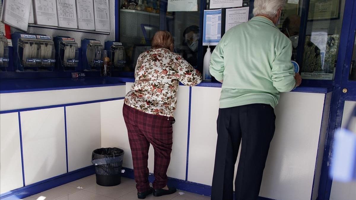 Un hombre y una mujer protegidos con mascarillas compran lotería en una Administración.