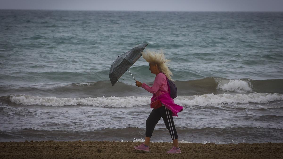 Una turista pasea por el Postiguet  un día de lluvia y viento