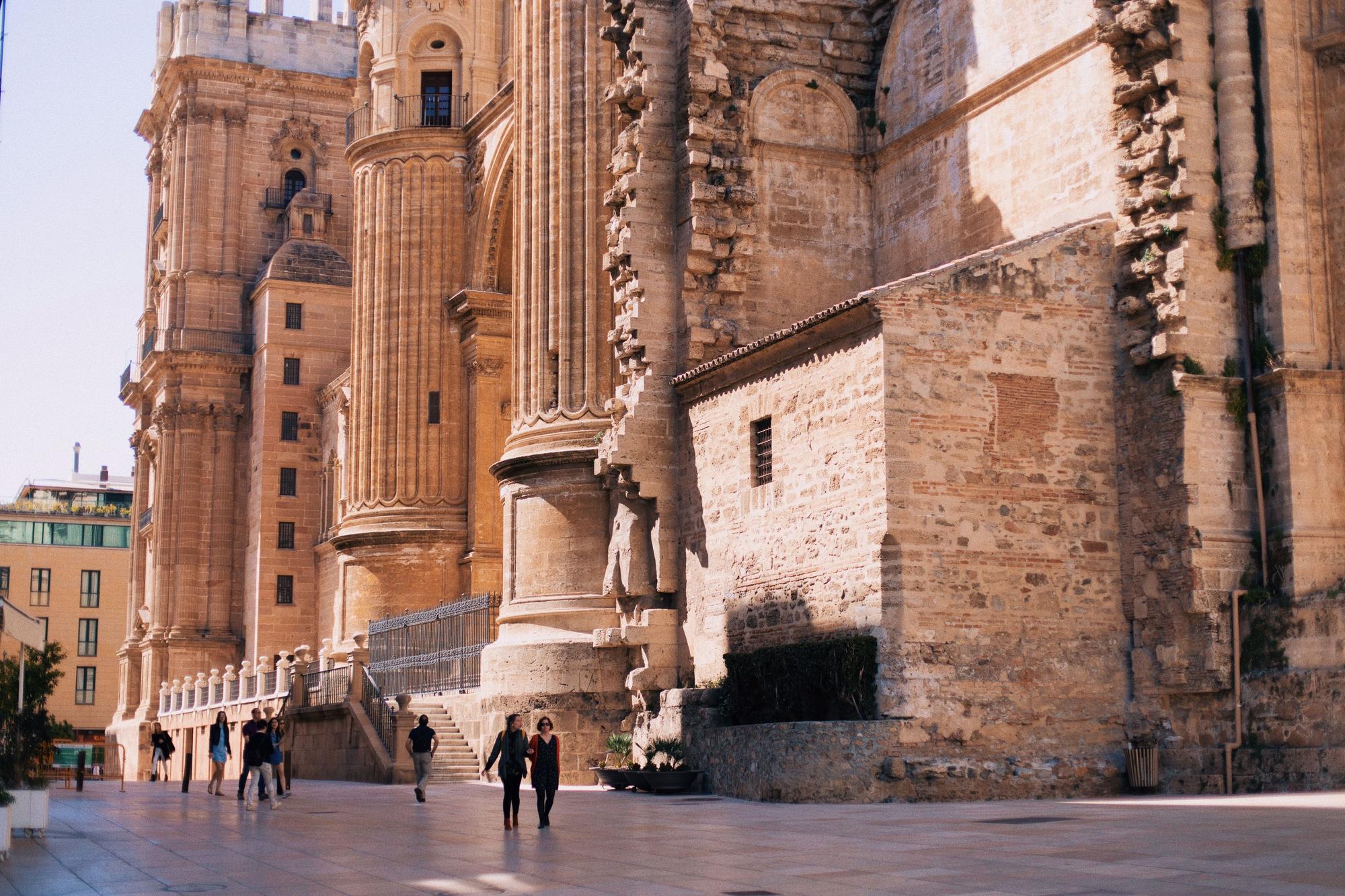 Dos personas caminan delante de la catedral de Málaga.