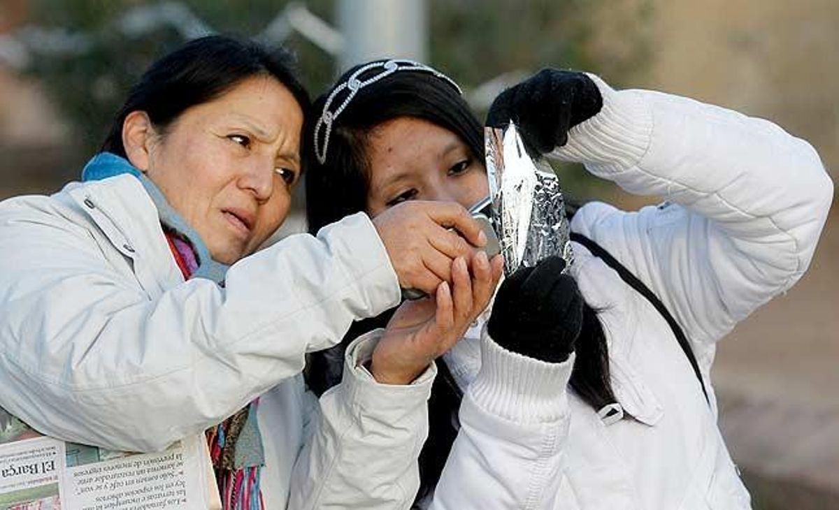 Dues dones miren de fotografiar l’eclipsi solar parcial que s’ha produït a primera hora d’aquest matí i que a Barcelona s’ha vist deslluït per la presència de núvols.
