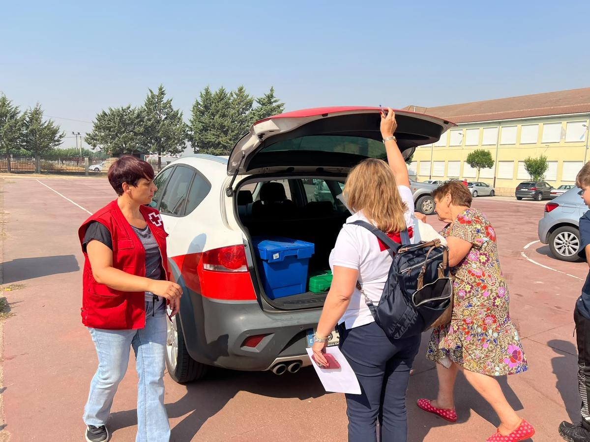 Personal de Cruz Roja ayudan a una vecina a guardar sus pertenencias en un vehículo para regresar al pueblo.