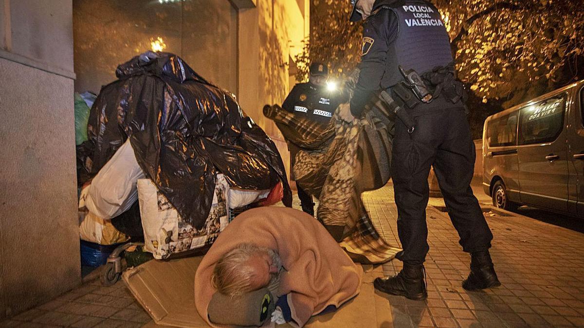 Dos agentes reparten mantas a un sintecho, en una fría noche en València. | LEVANTE-EMV