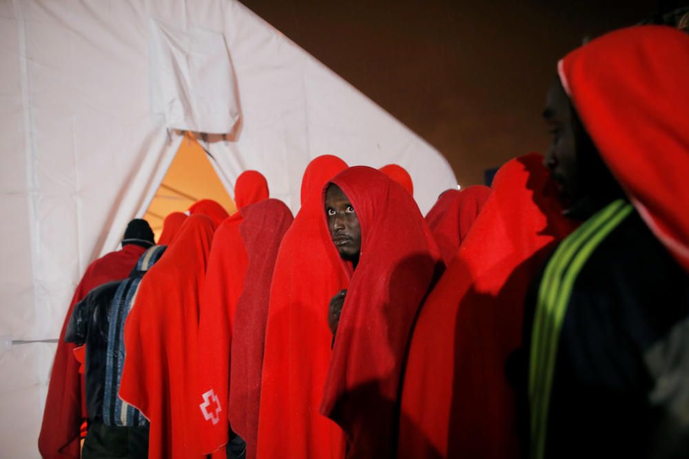 Migrants stand under the rain after disembarking ...