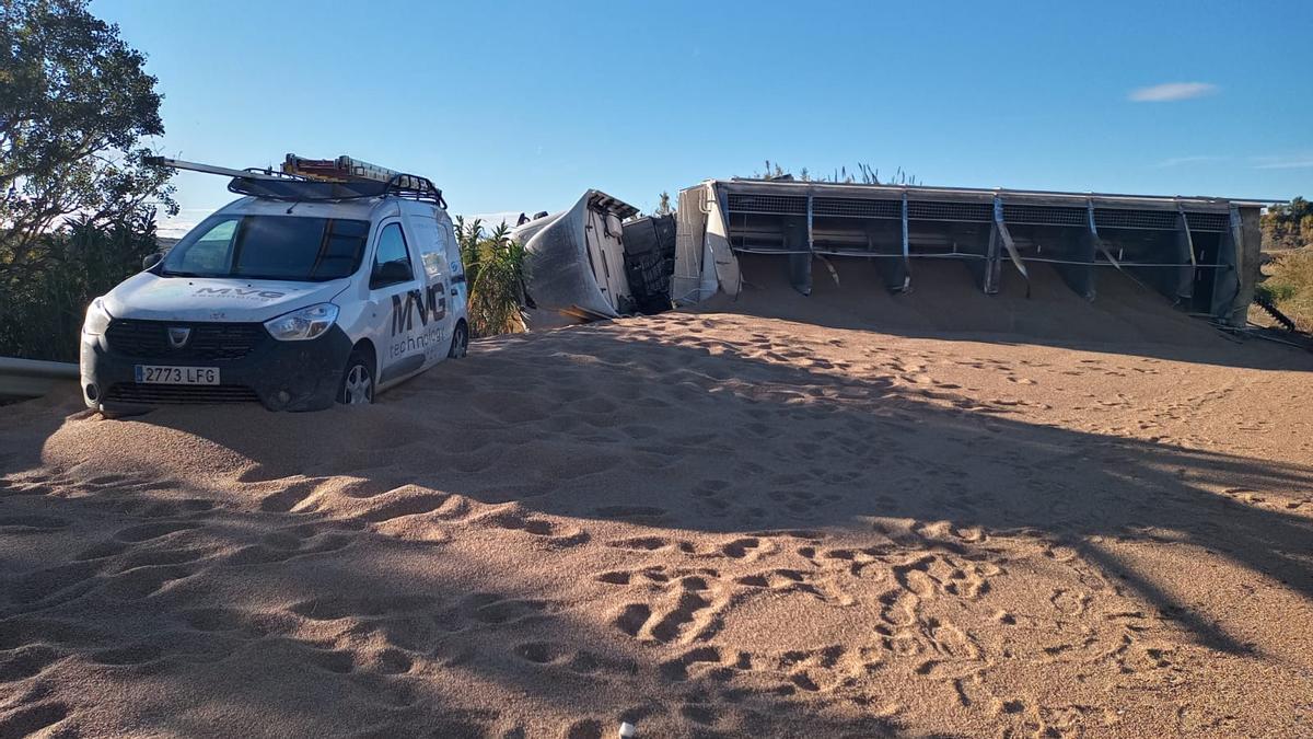 El cereal que transportaba un camión ha cubierto la carretera e impide el paso.