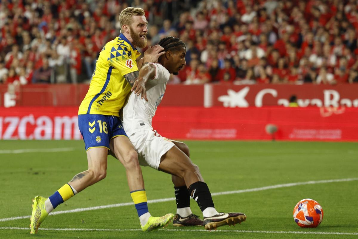 SEVILLA, 13/05/2025.- El defensa francés del Sevilla FC Loic Bade (d) lucha con el escocés Oliver McBurnie, de la UD Las Palmas, durante el partido de la jornada 36 de LaLiga que Sevilla FC y UD Las Palmas disputan este martes en el estadio Ramón Sánchez-Pizjuán. EFE/Julio Muñoz