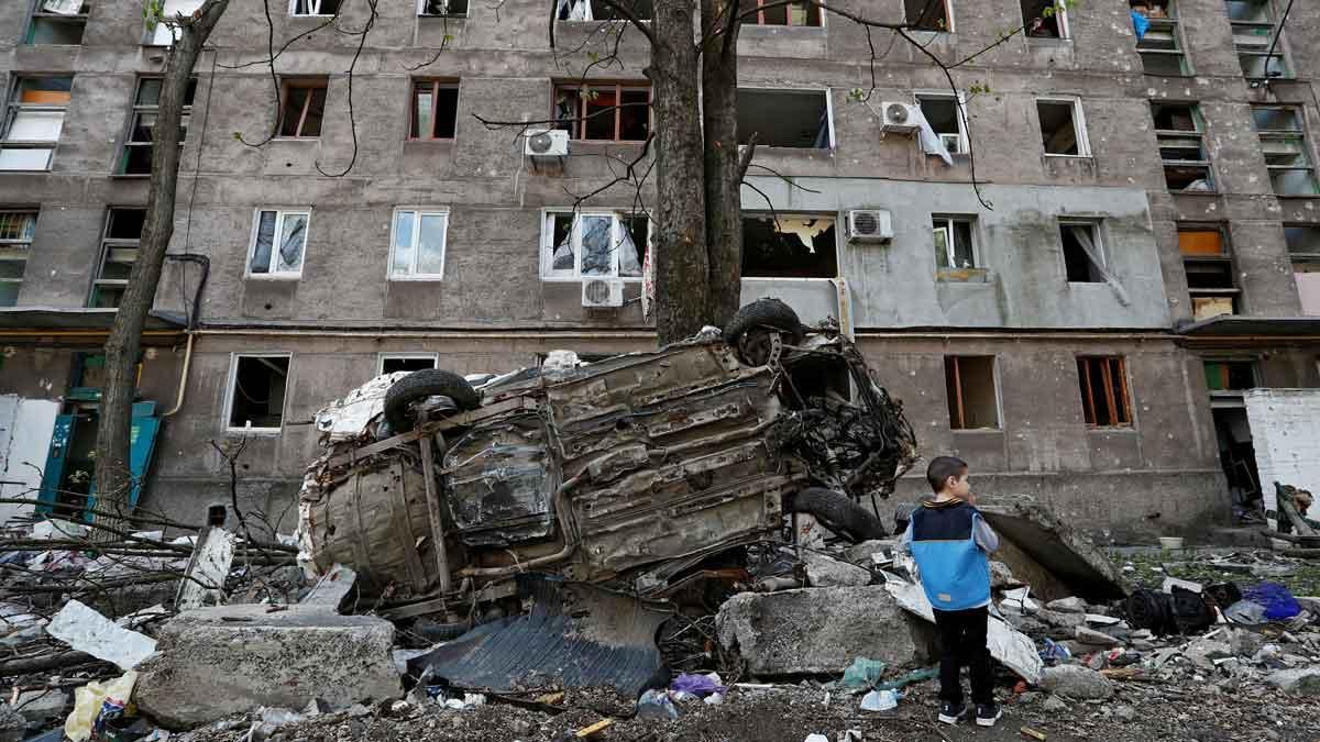 Un niño junto a un coche destrozado y un edificio de viviendas dañado por los ataques en la ciudad de Mariúpol. Un niño junto a un coche destrozado y un edificio de viviendas dañado por los ataques en la ciudad de Mariúpol.