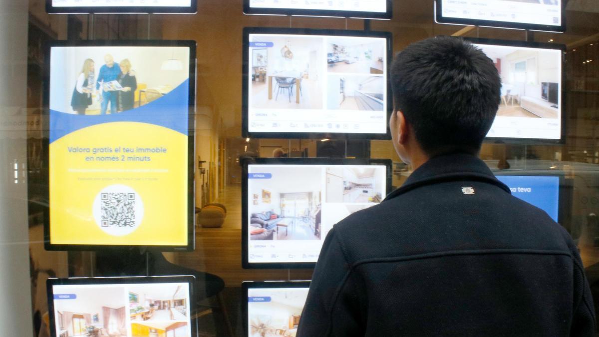 Un jove mirant anuncis a l'exterior d'una immobiliària de Girona