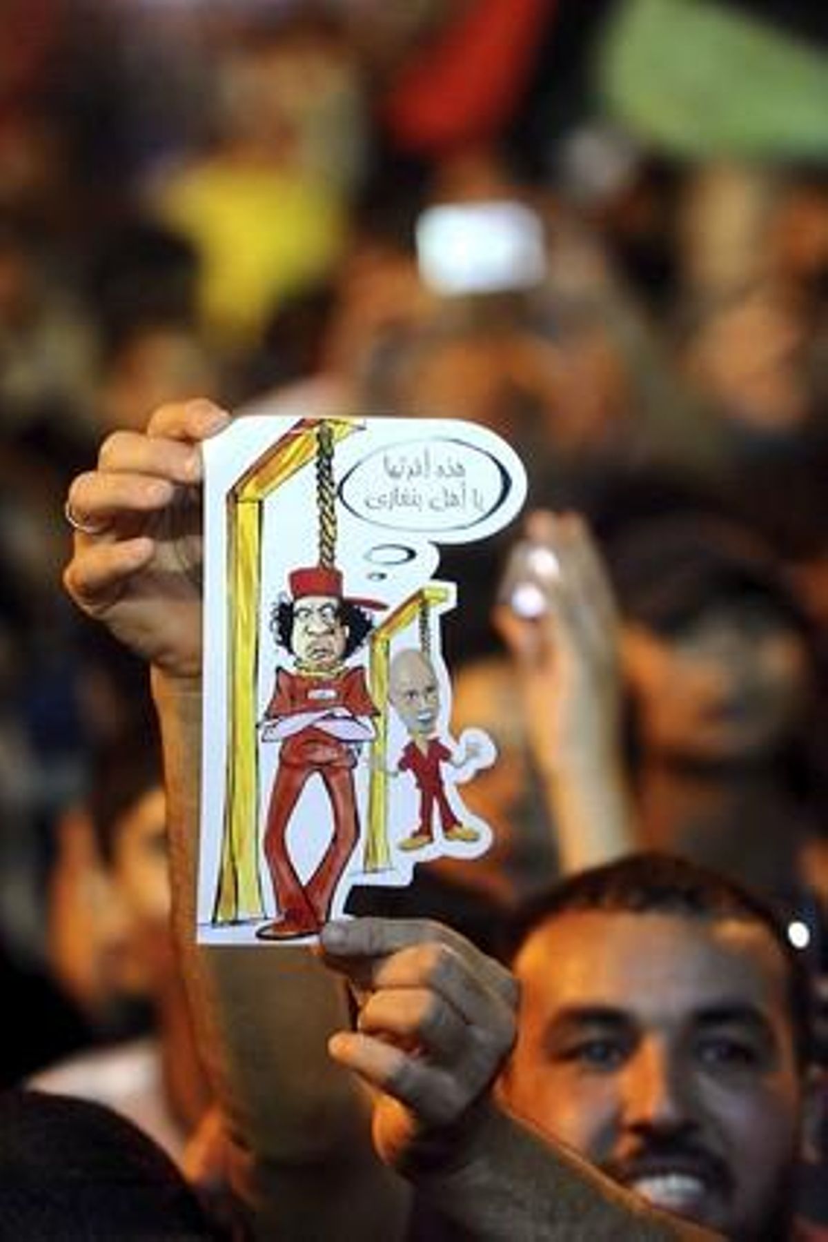Un home mostra una caricatura de Muammar al-Gaddafi penjat mentre celebra a Bengasi, amb una multitud de persones, l’ocupació de Trípoli.
