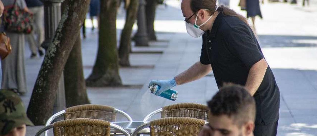 Un hombre desinfecta una mesa de una terraza en plena Calle Paseo. // Carlos Peteiro