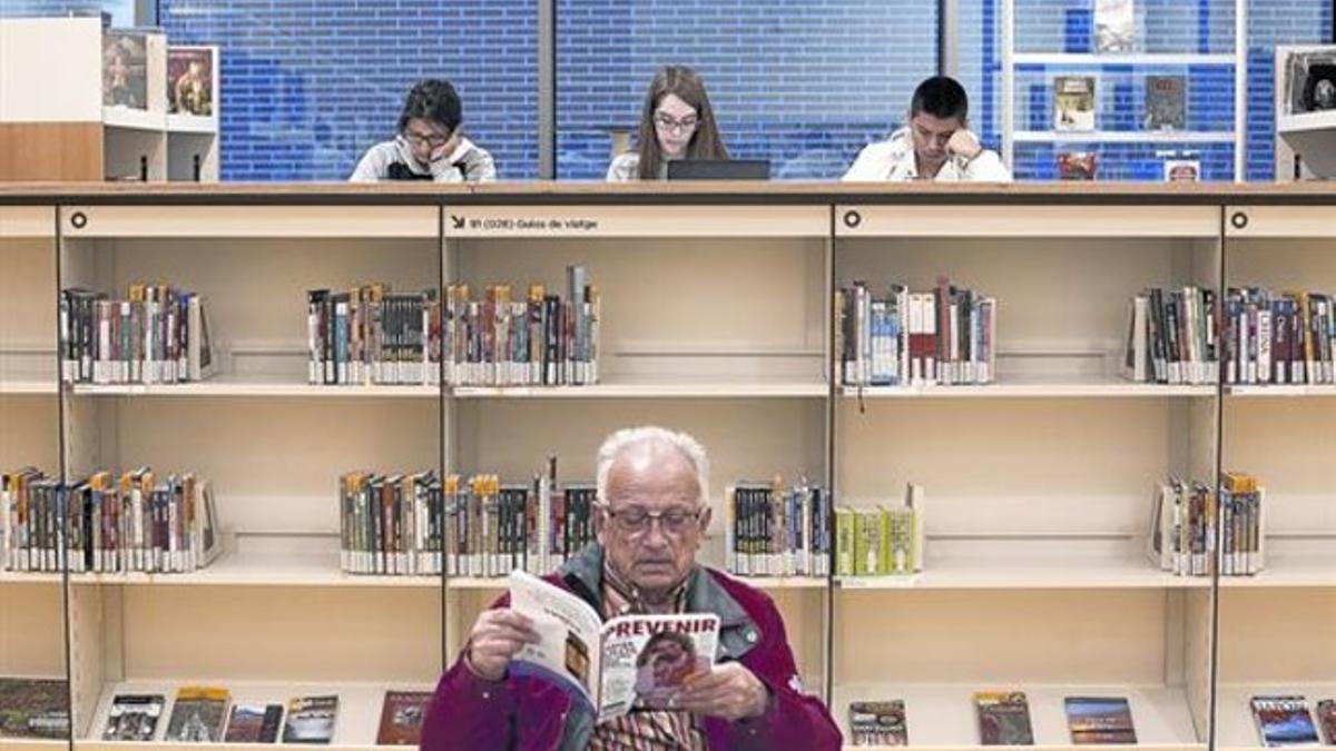 Un usuario de la Biblioteca de Sant Ildefons lee una revista mientras estudiantes de bachillerato preparan exámenes, el pasado jueves.