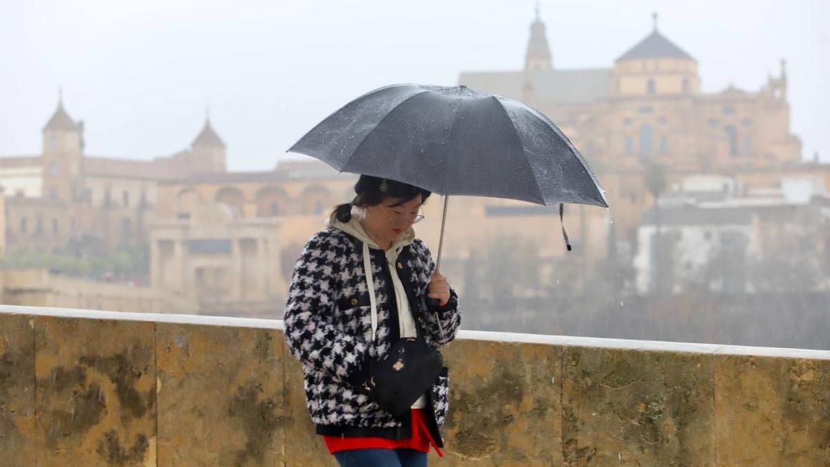 Una turistas pasea con paraguas por el Puente Romano de Córdoba ayer.
