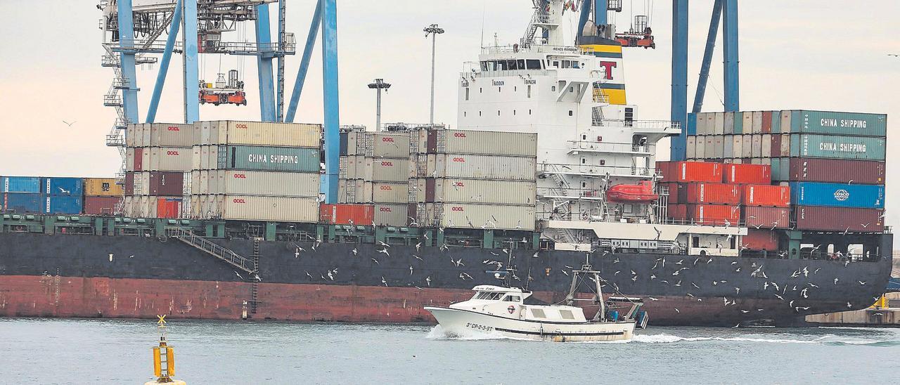 Un barco con contenedores, muchos de ellos de una compañía de transportes asiática, en el puerto de Castelló. En primer plano, una embarcación de pesca.