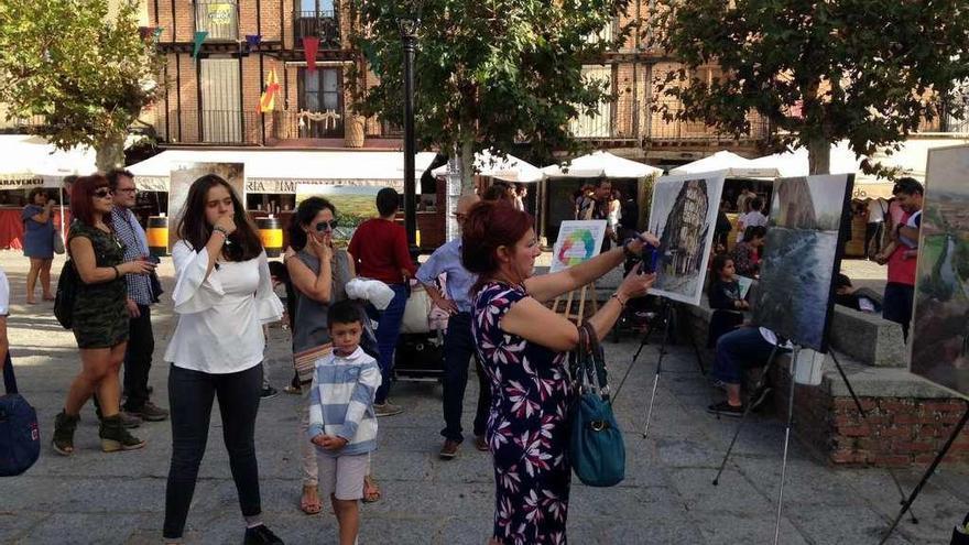 A la izquierda una mujer fotografía uno de los cuadros expuestos en la Plaza Mayor. Arrriba, el alcalde posa con los ganadores del certamen. A la derecha, una doncellas pasea por el mercado medieval.