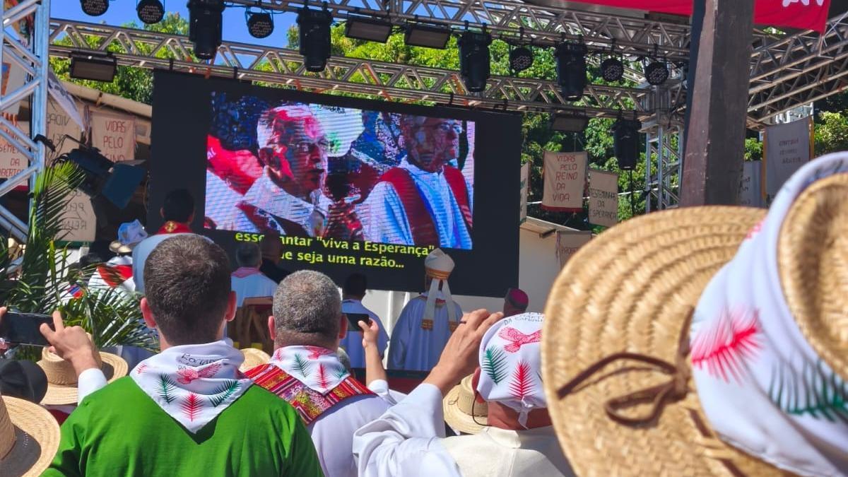 Assistents a la Romeria dels Màrtirs d’enguany davant d’una pantalla on es projecta una imatge on apareix Casaldàliga (a l’esquerra)