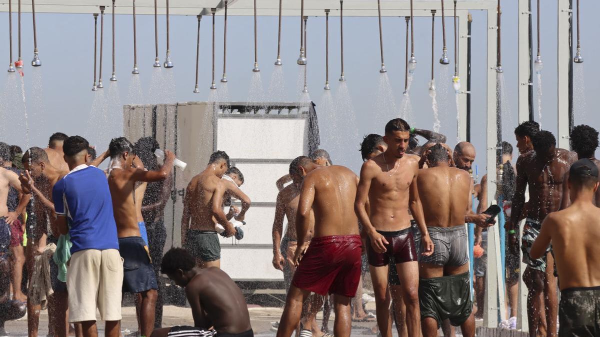 Migrantes se duchan en la playa de El Trampolín de Ceuta.