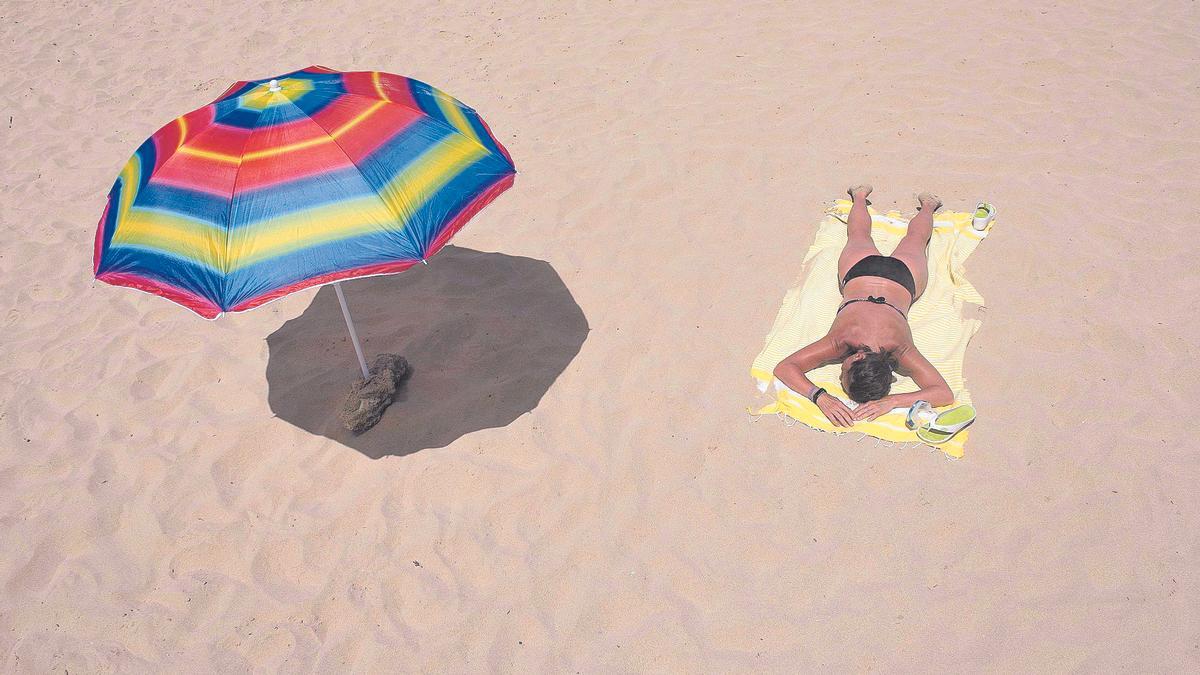 Una mujer se expone al sol, fuera de la sombrilla, en el Arenal d’en Castell, en la isla de Menorca.