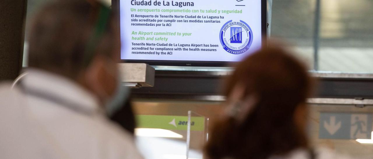 Dos usuarios del aeropuerto de Tenerife Norte miran un panel en el que se lee una recomendación sanitaria.