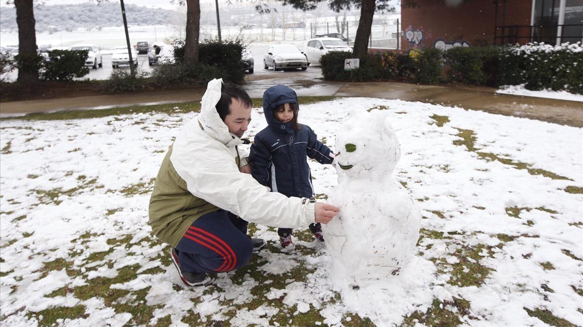 Padre e hijo construyendo un muñeco de nieve, en Maçanet de la Selva.