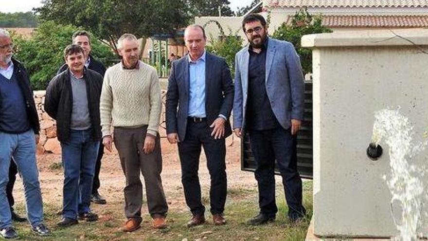 El agua de riego sale de una caseta de una de las fincas ante la mirada de los políticos, regantes y agricultores.