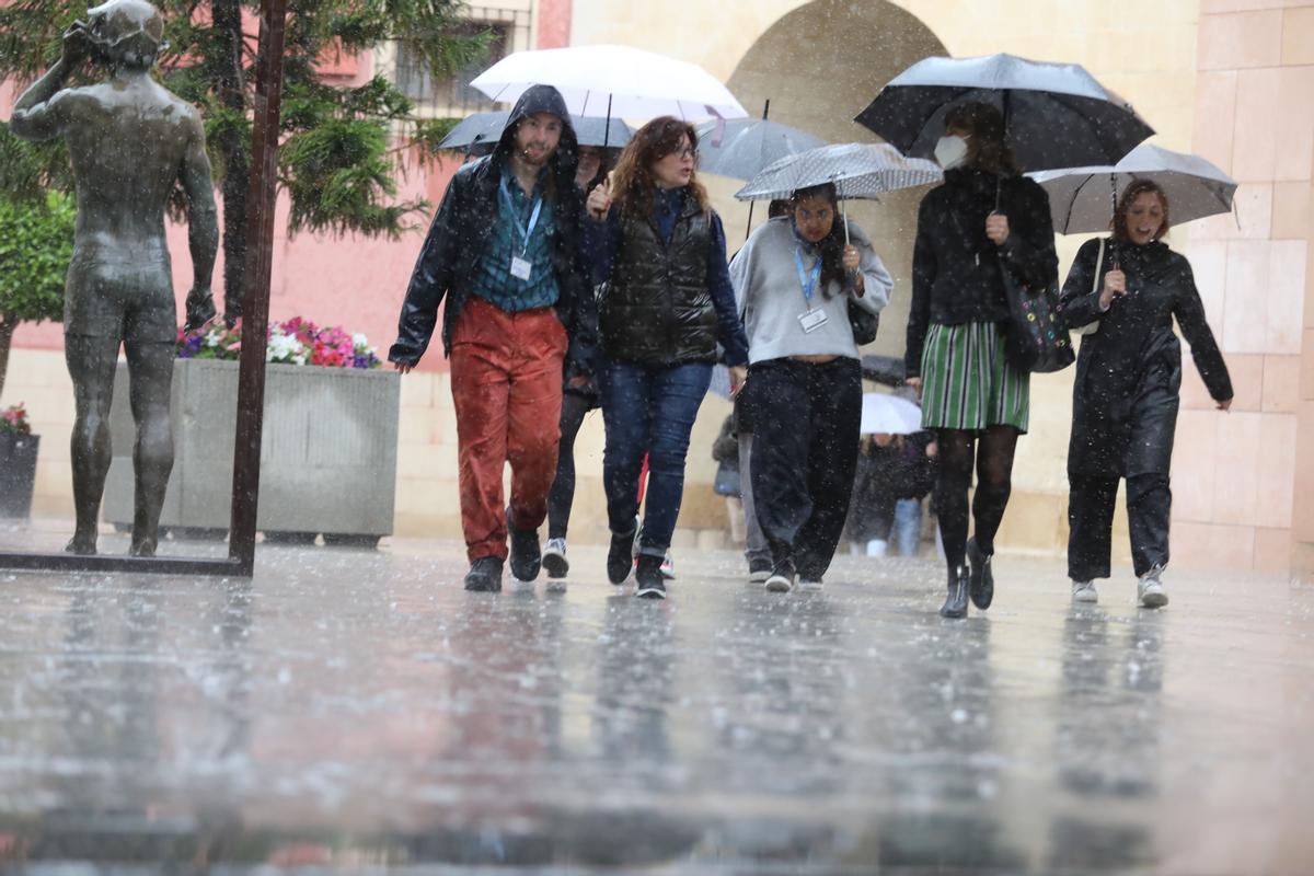 Varias personas caminando bajo la lluvia en Elche.