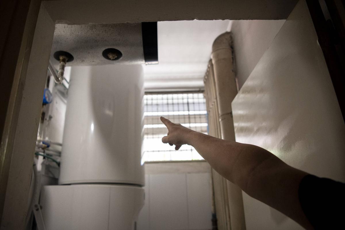 Un vecino señala la caldera del sistema de aerotermia instalado en su casa, que ocupa toda la estancia de la lavandería. Bloque de vivienda pública de la calle Tiana. Barcelona, 21 de agosto de 2026. Foto: Belén González / EP