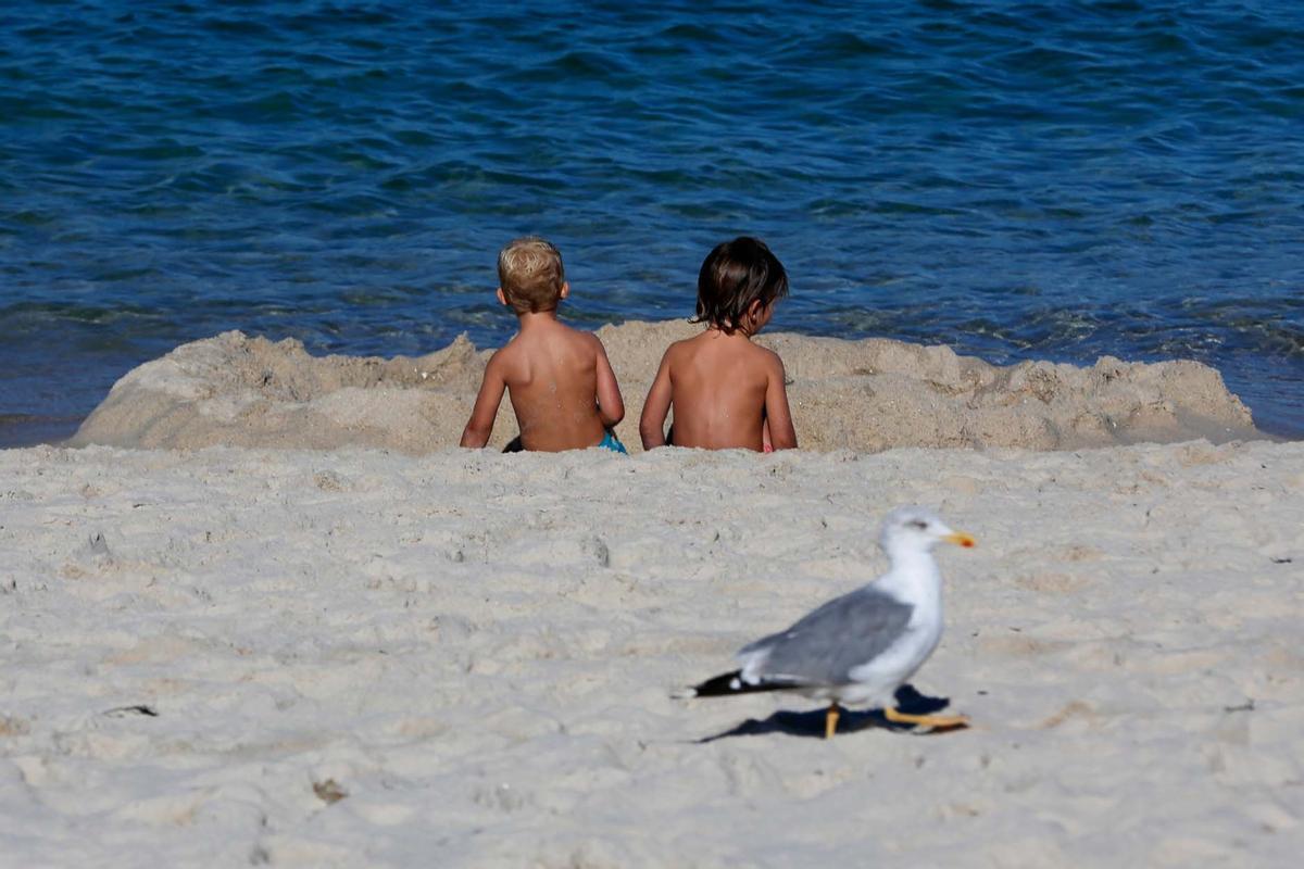 Dos niños de corta edad, sentados en la arena, en una playa.