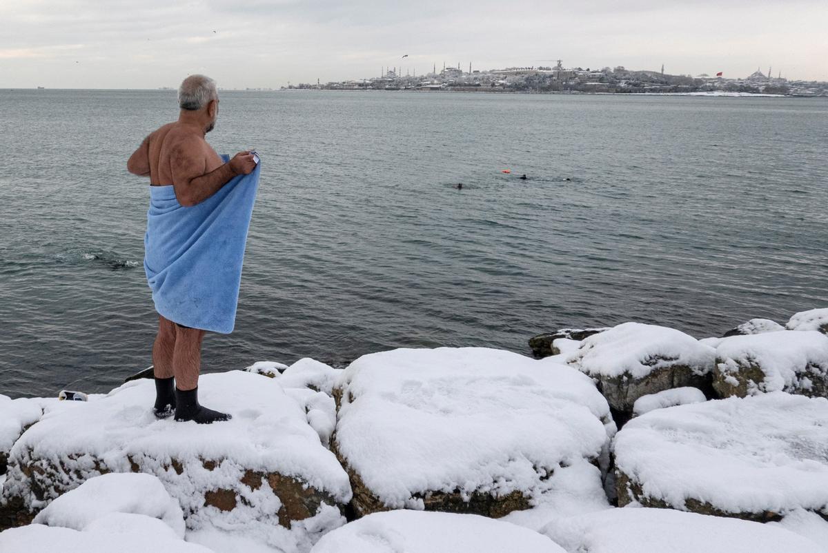 Un hombre se abriga con una toalla tras bañarse en el Bósforo. Al fondo, la mezquita Azul y Santa Sofía, en un día con abundante nieve en Estambul.