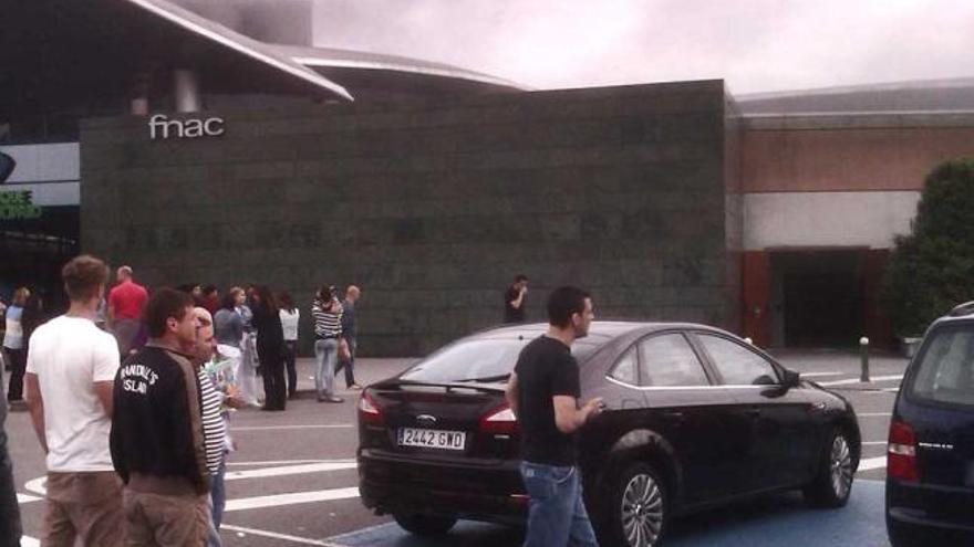 Clientes del centro comercial desalojados observan el humo sobre el tejado.